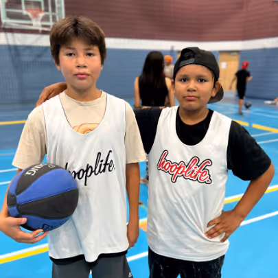 Two boys wearing white basketball jerseys with 'hooplife' standing in a gym with one holding a basketball.