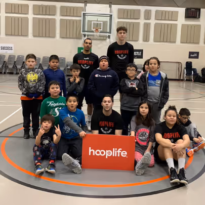 Group of children and two adults posing in a gymnasium around a red sign that says 'hooplife'.