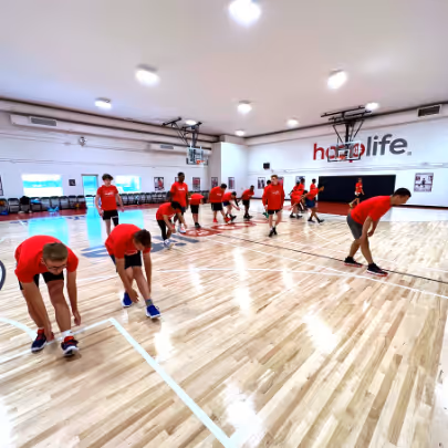 Young girl preparing to shoot a basketball in an indoor gym with other children playing in the background.