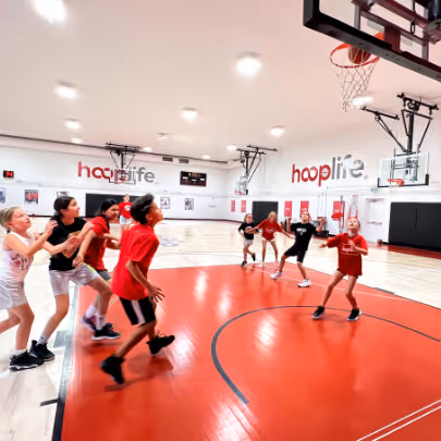 Children playing basketball indoors on a red and white court with 'hooplife' written on the walls.