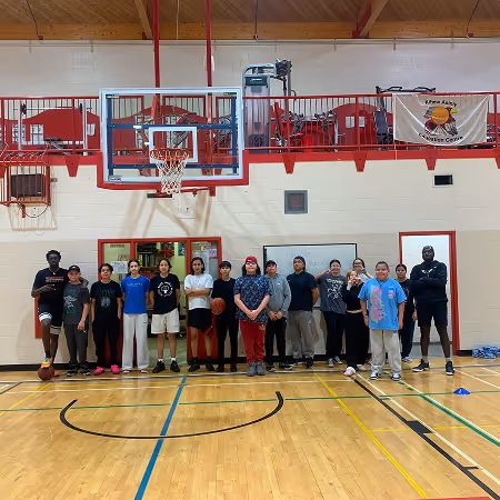 Group of diverse teenagers standing in a line on a gym basketball court under a hoop.