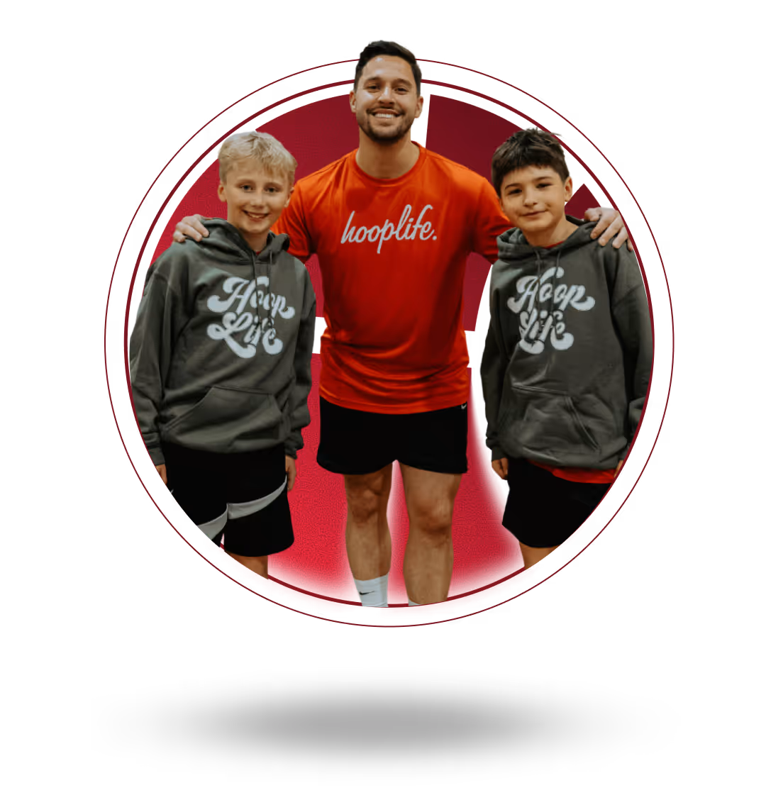 Smiling adult man in red 'hooplife.' shirt with arms around two boys wearing gray 'Hoop Life' hoodies and black shorts.